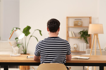 Wall Mural - Home workplace. Man working at wooden desk in room, back view