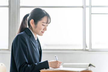 学校の教室で数学の教科書・参考書を見ながら勉強する女子高校生・中学生の生徒
