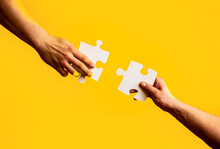 Business Solutions, Success And Strategy Concept. Two Hands Trying To Connect Couple Puzzle With Yellow Background. Closeup Hands Of Man Connecting Jigsaw Puzzle