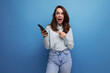 25 year old brunette woman uses a smartphone in her hand on a blue background with copy space