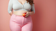 Beautiful Overweight Woman Dressed In Pink Overalls Holding An Apple On A Pink Background. Healthy Lifestyle And Self-acceptance. Evoking Only Positive Emotions