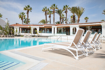 Clean and fresh resort swimming pool lined with comfortable sunbeds prepared for tourists to enjoy the summer vacation days at The Club, Amarilla Golf, Tenerife, Canary Islands, Spain 