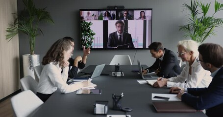 Canvas Print - Business group meeting at conference table, looking at large display with head shots of speaking colleagues, using Internet technology for remote teamwork. Boss talking to team on video call