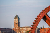Red industrial gears with nineteenth century brick mill building in background in Lawrence, Massachusetts.