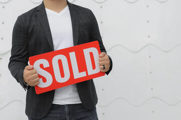 Wall Mural - man in a business casual attire clothes holding up a sold sign