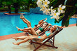 Portrait of stunning sexy women taking sunbaths on lounges, with legs up near swimming pool
