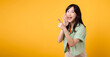 Capture engagement and excitement with Asian young woman wears pastel green shirt on orange shirt show happy smile while placing hand over mouth and pointing with a finger to free copy space.