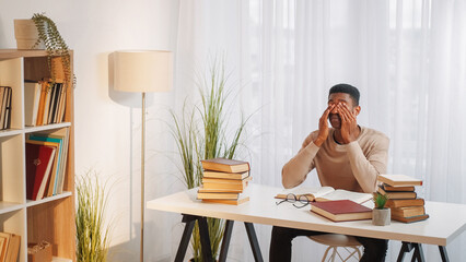 Wall Mural - Education stress. Hard exam. Difficult study. Exhausted man with eyestrain pain reading book preparing homework research at home desk copy space.