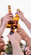 © CarlosBarquero - Cheerful young friends toasting together with beer. Happy diverse people clinking bottles outdoors at spring party in the park. Multiracial group having fun and celebrating friendship in community.