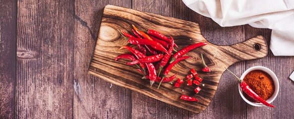 Crushed red hot peppers and whole peppers on a wooden board top view web banner