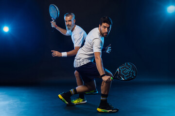 Wall Mural - Padel tennis doubles. Two athletes players with racket. Man athlete with paddle racket on court with neon colors. Sport concept. Download a high quality photo for the design of a sports app