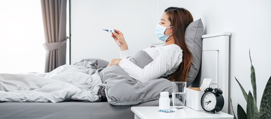 Asian woman in medical face mask feeling sick and holding thermo