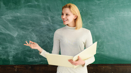 Wall Mural - Education in high school university college. Back to school. World teachers day. Smiling female teacher with notebook standing near blackboard giving lesson. Happy student or teacher in classroom.