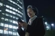 © InfiniteFlow - a senior chinese japanese businesswoman executive using mobile phone with background of modern office buildings at night Generative AI AIG18.