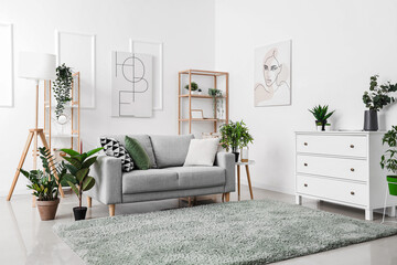 Interior of light living room with cozy grey sofa and green houseplants