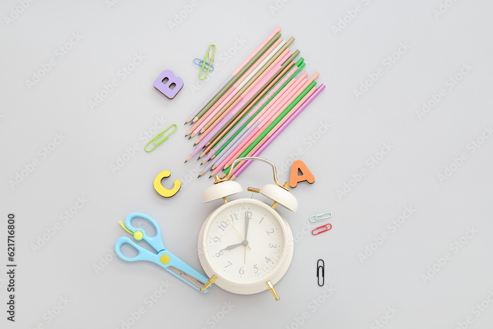 Alarm clock with wooden letters and different stationery on grey background