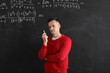 Male Math teacher with chalk piece near blackboard in classroom