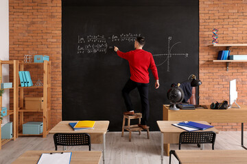 Male Math teacher writing equation on blackboard in classroom