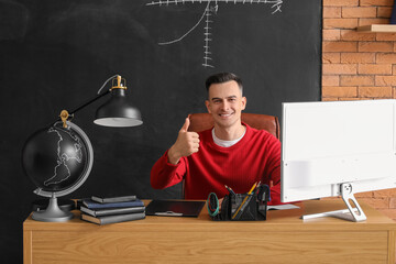 Canvas Print - Male teacher showing thumb-up at table in classroom