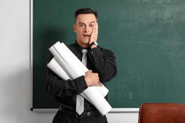 Poster - Surprised male teacher with rolls of paper near chalkboard in classroom