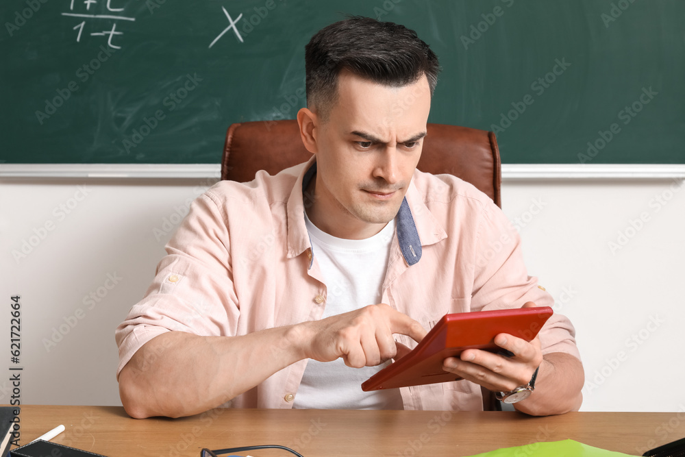 Male Math teacher with calculator sitting at table in classroom