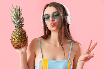 Poster - Young woman in headphones with pineapple blowing kiss on pink background