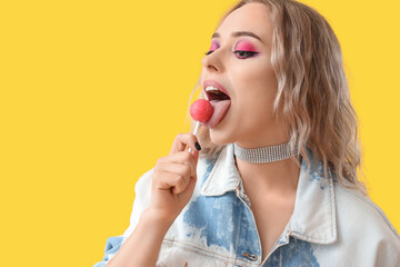 Poster - Young woman eating lollipop on yellow background, closeup