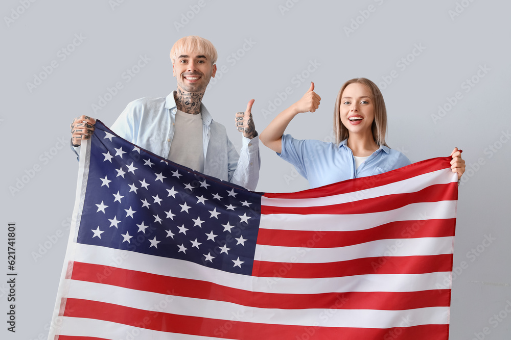 Young couple with USA flag showing thumbs-up on light background