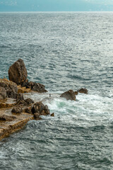 Ocean waves braking at coastline rocks covering them in white sea foam on sunny summer day