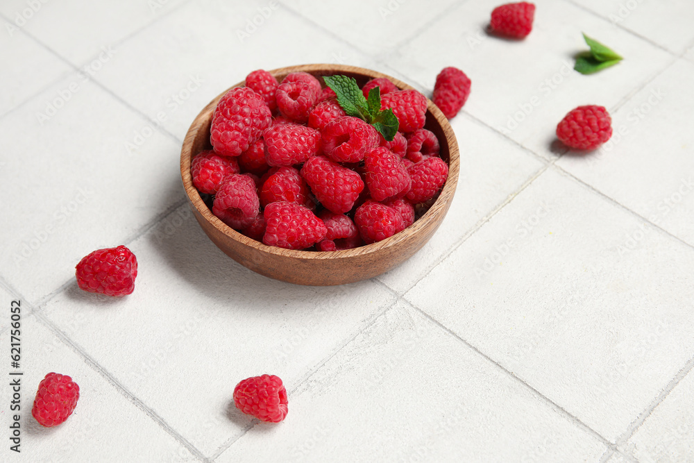 Bowl with fresh raspberry and mint on light tile background, closeup