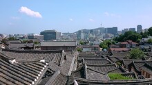 한국 서울 북촌한옥마을을 드론으로 한옥의 기와 지붕 사이를 통과하며 촬영, 멀리 남산과 맑은 하늘, 서울의 도심이 보인다