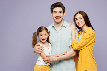 Wall Mural - Young happy cheerful parents mom dad with child kid daughter girl 6 years old wear blue yellow casual clothes look camera hug cuddle together isolated on plain purple background. Family day concept.