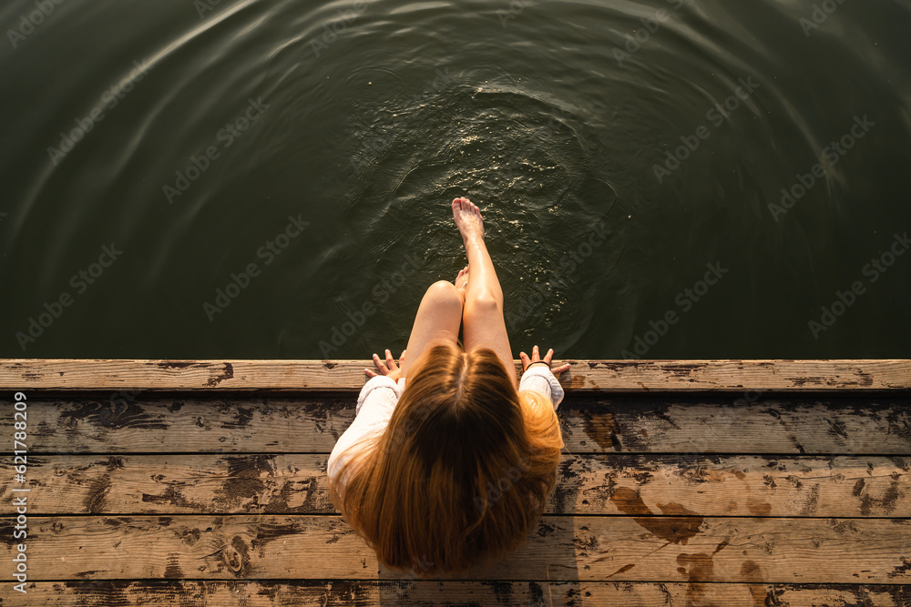 Woman relaxes by the lake sitting on the edge of a wooden jetty, swing ...