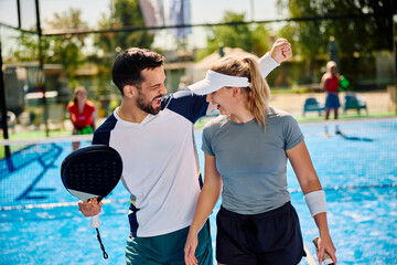 Cheerful athletic couple celebrates during padel tennis match on outdoor court.