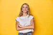 © Asier - Young blonde Caucasian woman in a white t-shirt on a yellow studio background, who feels confident, crossing arms with determination.