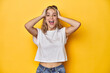 © Asier - Young blonde Caucasian woman in a white t-shirt on a yellow studio background, screaming, very excited, passionate, satisfied with something.