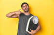 © Asier - Sporty Caucasian man hugging a scale on a yellow studio background.