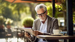 Portrait of modern senior man reading news using ebook in outdoor cafe. Digital ink technology
