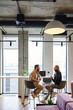 © LIGHTFIELD STUDIOS - side view of ambitious business colleagues talking about new startup project near laptop in modern office with large windows and high tech interior, productivity and collaboration concept