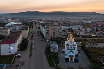 Wall Mural - Aerial view of the city at dawn. Morning cityscape. Top view of the church, buildings and an empty street. Church of Saint John the Baptist, city of Magadan, Magadan region, Siberia, Far East Russia.