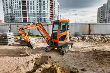 Fototapete - A small mini excavator is working on a construction site. Close-up. View from above. Work in cramped conditions. Excavation.