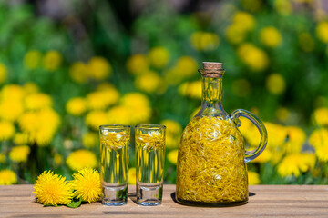 Wall Mural - Homemade dandelion flowers tincture in two glasses and in a glass bottle on a wooden table in a summer garden, closeup