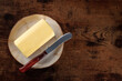 A block of butter with a knife on a plate, shot from above a dark rustic wooden background with copy space
