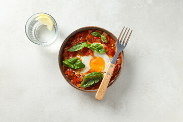 Wall Mural - Shakshuka in bowl, fork and glass of water on light background, top view