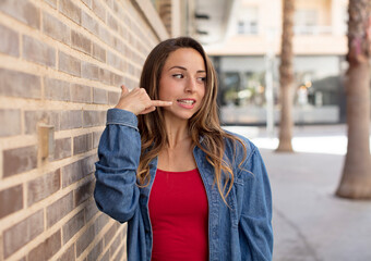 Wall Mural - pretty woman smiling cheerfully and pointing to camera while making a call you later gesture, talking on phone