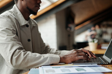 Aufkleber - Cropped shot of young African American male economist analyzing online financial data while sitting by workplace in office in front of laptop