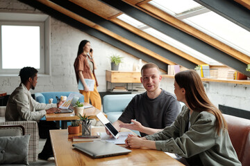 Confident young male employee pointing at tablet screen during explanation of online data to female colleague in coworking space