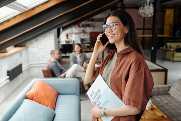 Aufkleber - Young successful female manager or office worker with financial documents in hand talking on smartphone against two colleagues