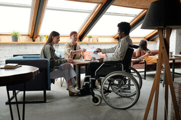 Aufkleber - Young African American male economist with disability passing document to colleague over workplace during discussion of financial information