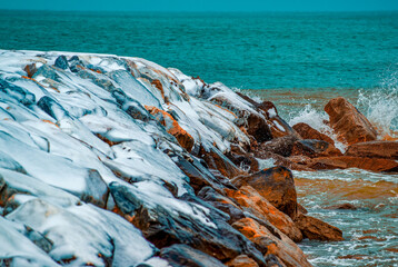 Canvas Print - Rocks above the sea covered in snow after a snowstorm. Weather and climate change concept